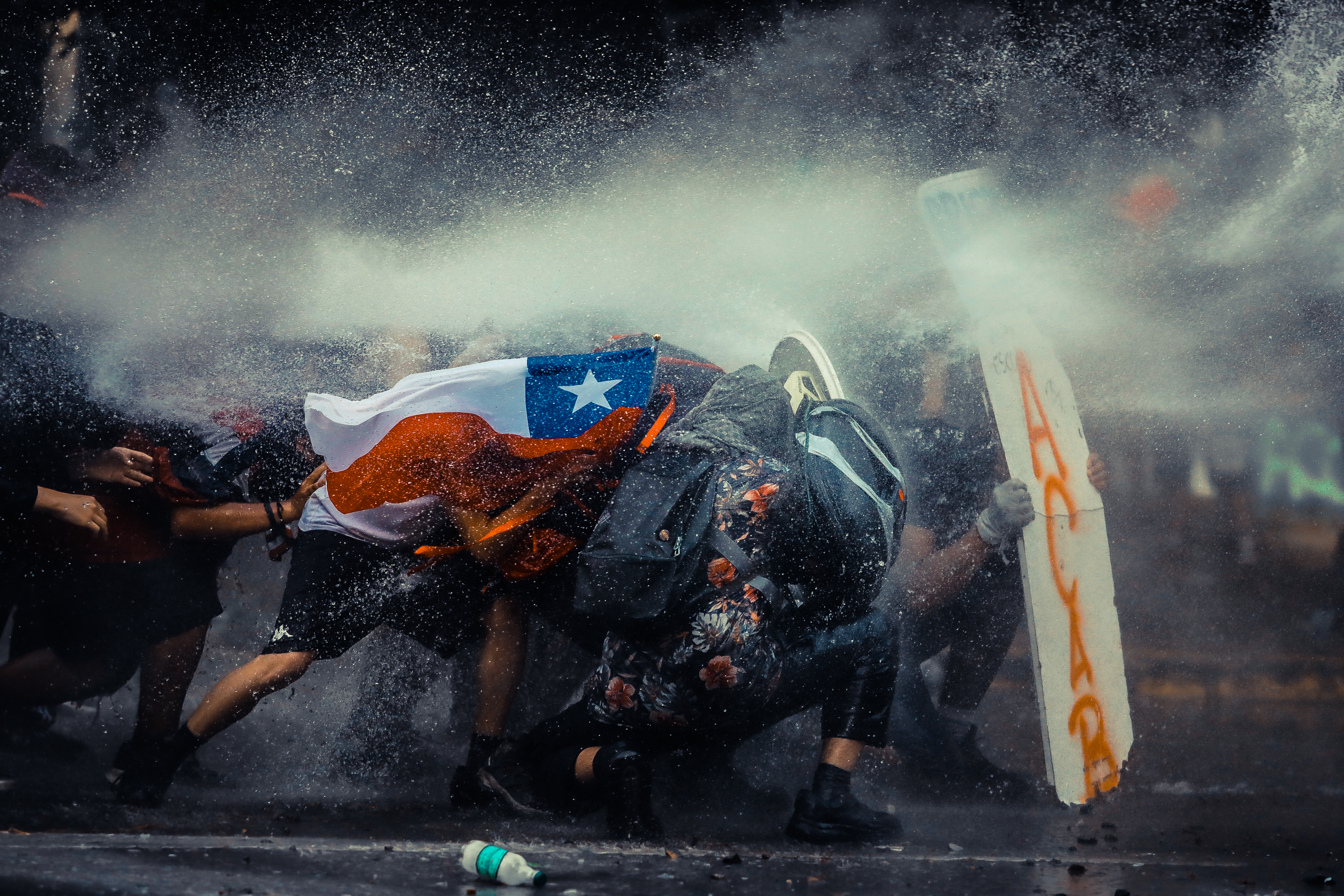 Manifestantes se protegen del carro lanza agua (guanaco) de FFEE de carabineros durante la cuarta semana de protestas en Chile el 11 de Noviembre de 2019. Manifestantes se protegen del carro lanza agua (guanaco) de FFEE de carabineros durante la cuarta semana de protestas en Chile el 11 de Noviembre de 2019.