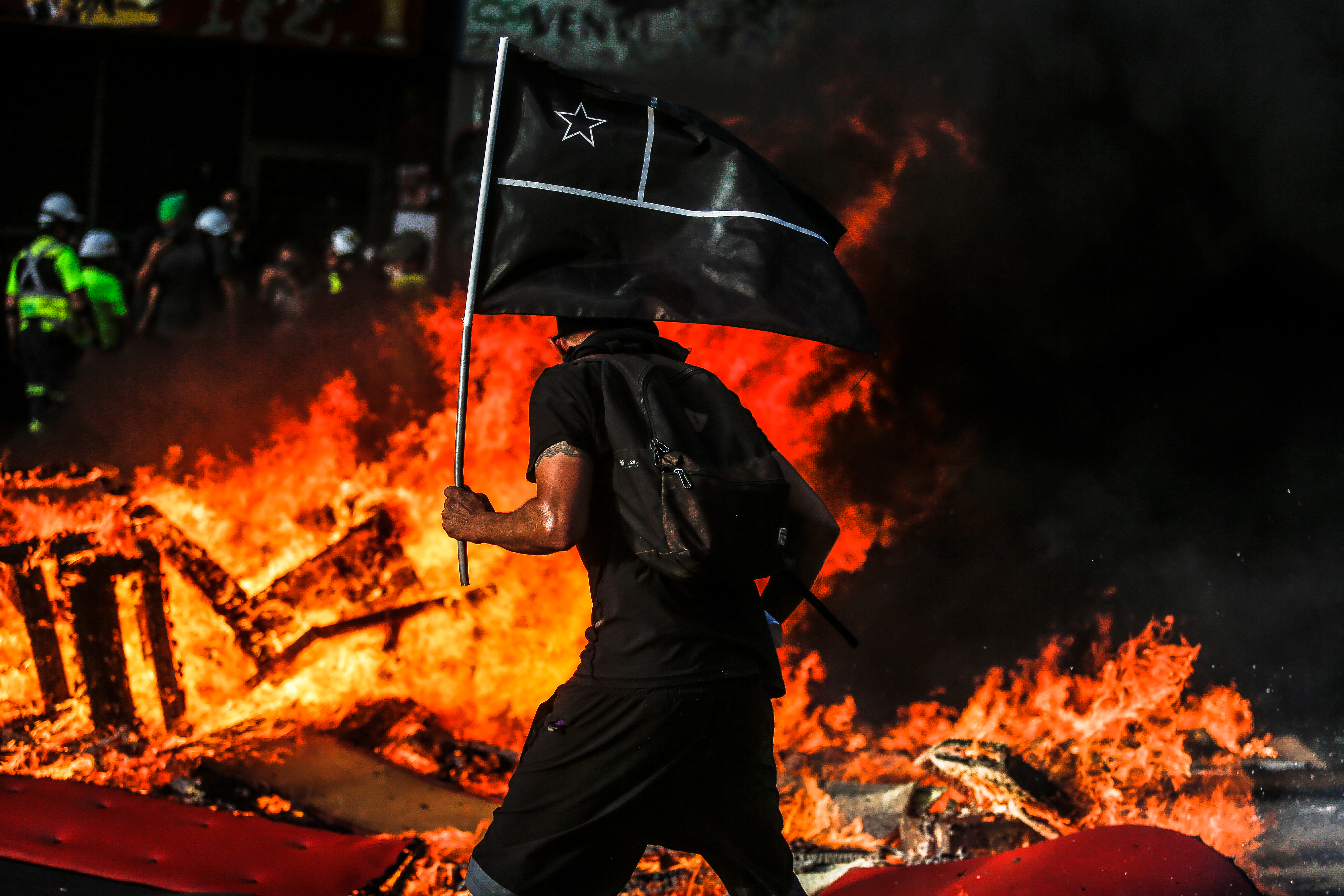 Un manifestante con una bandera de Chile de color negra pasa por una barricada en la arteria principal de la comuna de Santiago el día 28 de Noviembre de 2019. Un manifestante con una bandera de Chile de color negra pasa por una barricada en la arteria principal de la comuna de Santiago el día 28 de Noviembre de 2019.