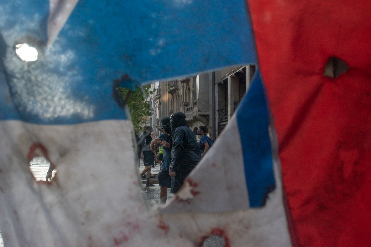 Manifestantes atraviesan bandera chilena marcada con agujeros en contexto de jornada de protesta, 13 de Enero 2020, Santiago. Manifestantes atraviesan bandera chilena marcada con agujeros en contexto de jornada de protesta, 13 de Enero 2020, Santiago.