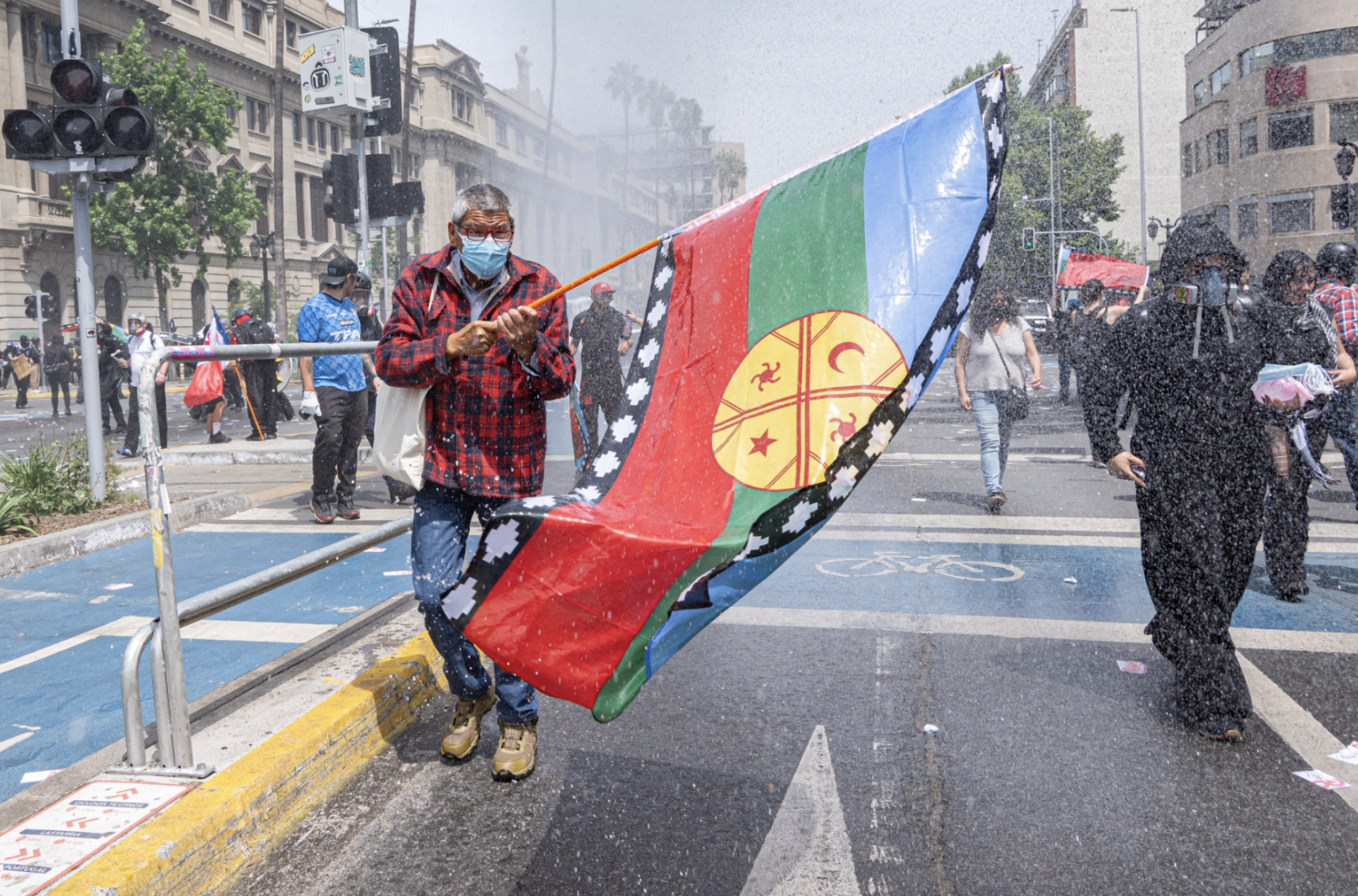 Un manifestante lleva la bandera mapuche mientras lo golpean con un cañón de agua en Av. Libertador O’Higgins. (Foto: Ike Wood / Interferencia.cl)