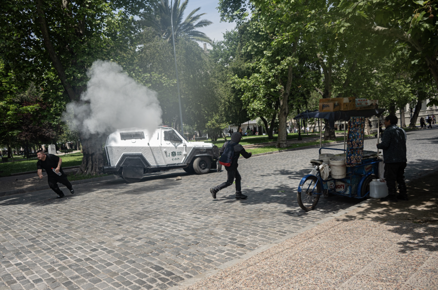 Un vendedor callejero mira mientras un vehículo de fuerzas especiales acelera a través del Parque Forestal. (Foto: Ike Wood / Interferencia.cl)